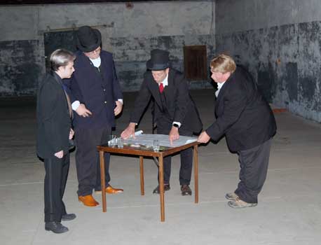Four men stand around table.